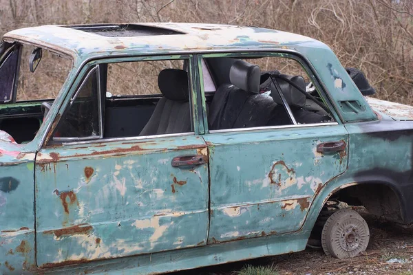 Eski, yeşil, parçalanmış bir yolcu arabası sokakta duruyor.