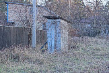 Eski bir kırsal ahşap tuvalet, sokaktaki kuru çimenlerin içinde, yerde duruyor.