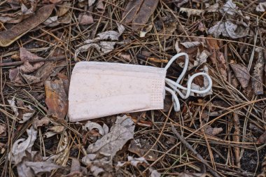 Eski bir pembe tıbbi maske, sokakta gri zeminde yatıyor.