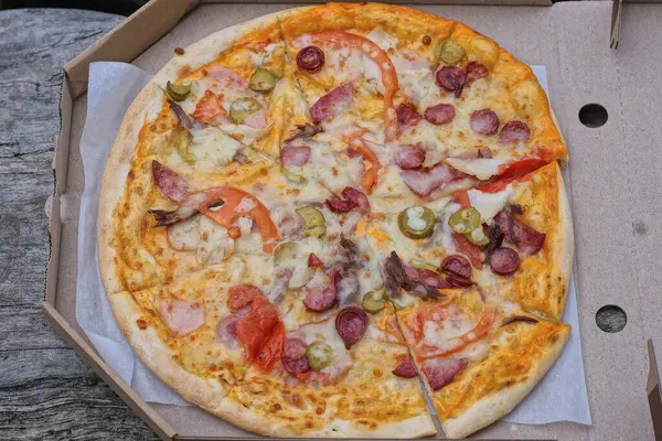 food and one round colored pizza carbonara in a gray paper carton box in the street