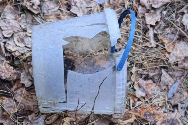 Kırık beyaz plastik bir kovanın çöpü, sokaktaki kuru çimenlerin içinde gri zeminde yatıyor.
