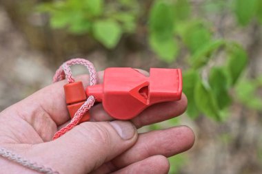 Elinde kırmızı plastik bir düdük, caddedeki bir ipte.