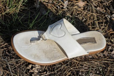 Beyaz deri bir sandalet sokağın gri zemininde yatıyor.