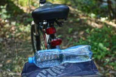 Mavi plastik bir şişe su, sokaktaki siyah bir bisikletin rafında duruyor.