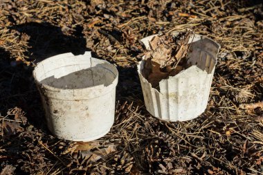 İki beyaz, eski, kirli plastik saksı dışarıda, yerde duruyor.