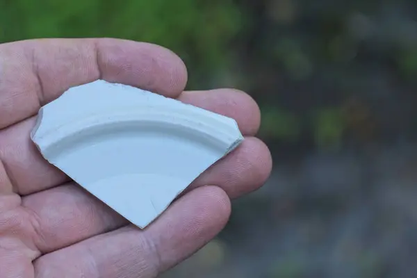 stock image hand holding a piece of white small old ceramic tile on the street