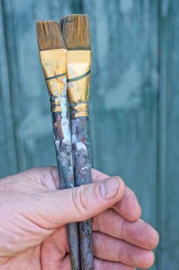 Yeşil arka planda iki kirli siyah boya fırçasıyla el ele tutuşuyorlar.