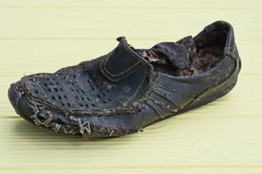 Sarı ahşap bir masanın üzerinde dikişli bir deliği olan eski siyah yırtık deri bir bot var.