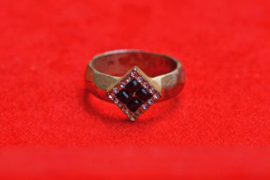 Mor taşlı sarı bir yüzük kırmızı masada yatıyor.