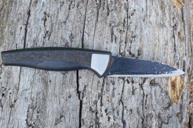 Gri ahşap bir masada küçük siyah bir bıçak yatıyor.