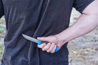 Siyah elbiseli bir erkek suçlunun eli ve sokakta arkasından gri bir bıçak.