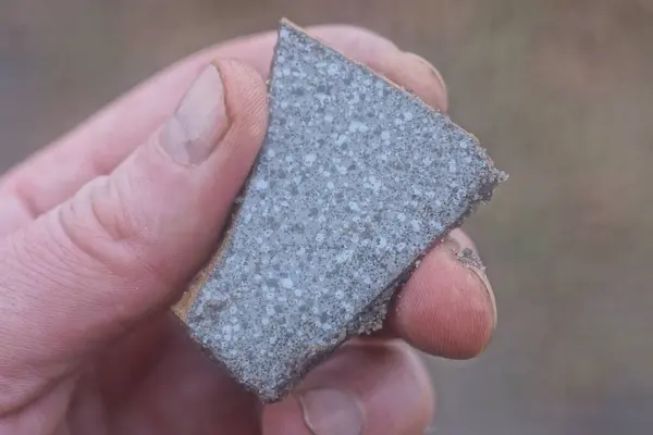 stock image hand holding a piece of small old gray ceramic tile on the street