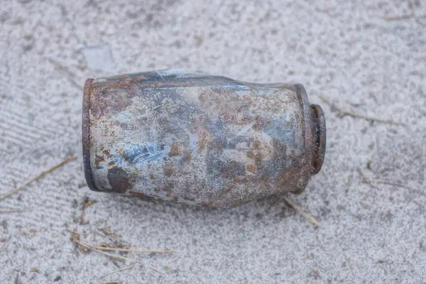 stock image one old rusty burnt metal can lies on the gray sand on the street