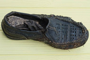 Sarı ahşap bir masanın üzerinde eski siyah yırtık bir deri bot yatıyor.