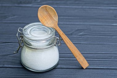 Bir kavanoz beyaz şeker ve siyah masada kahverengi tahta kaşık.