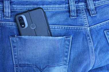Siyah, gri bir akıllı telefon, pamuk pantolonun mavi cebinde sokaktaki bir adamın üzerinde duruyor.