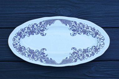 Mavi desenli boş bir seramik beyaz oval tabak siyah ahşap masa üzerinde duruyor.