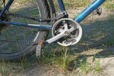 Siyah bisiklet pedalı metal bir kazıkta, mavi spor bisikletinin zinciri caddede yeşil çimlerde.