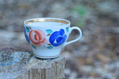 Kırmızı mavi çiçek desenli beyaz seramik bir bardak caddedeki gri bir masada duruyor.