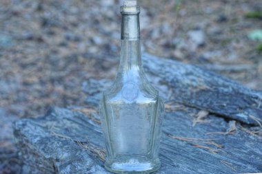 Sokakta bir kütüğün üzerinde duran büyük, kirli bir cam şişe.