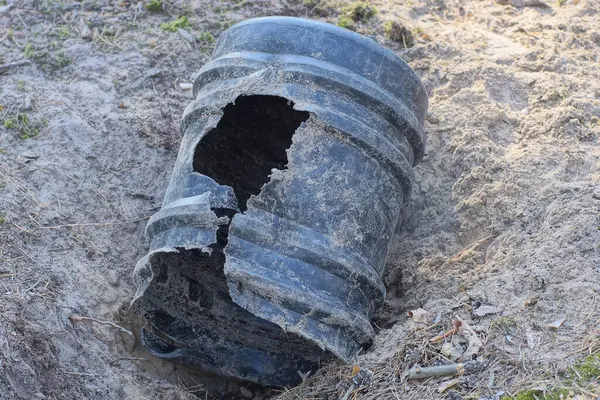 Büyük, eski, kırık bir plastik fıçı. Sokakta gri bir kum çukurunda bir delik var.