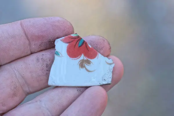 stock image hand holding a piece of small old color ceramic tile  on the street