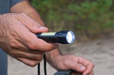 El, sokağın gri arka planında parlak bir siyah metal el feneri tutuyor.