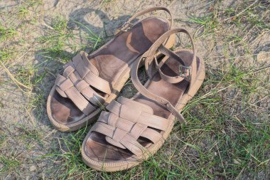 İki deri kahverengi sandalet gri zeminde ve yeşil çimenler doğada duruyor.