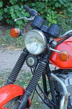 Beyaz camlı far ve siyah gidonu olan eski bir motosikletin parçası. Bir yaz caddesinde kırmızı benzin deposunun yanında.