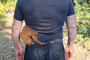 Mavi siyah elbiseli bir erkek işçi. Bir yaz caddesinde, kemerinde eski, paslı kahverengi bir kürek var.