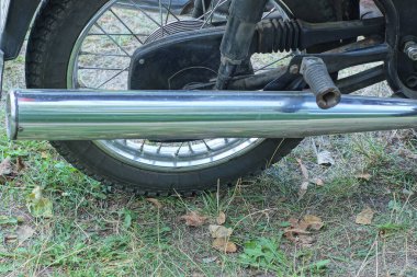 Uzun gri metal egzoz borusu yaz caddesinde yeşil çimlerin üzerinde eski motorsikletin siyah tekerleğinin yanında.