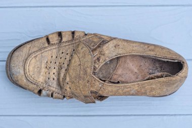 Gri ahşap bir masada eski kahverengi yırtık bir deri bot yatıyor.