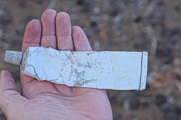 stock image one old metal small white tube lies on the palm of a hand on a summer street