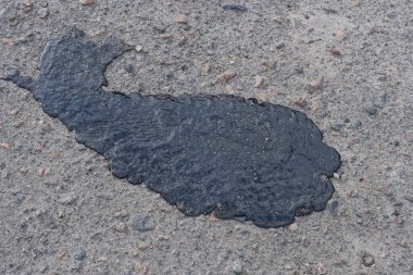 Bir yaz caddesinde yolun gri asfaltında büyük siyah bir reçine lekesi.