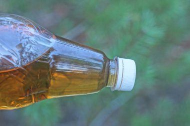 Bir plastik şişe beyaz mantarla kaplanmış, yeşil arka planda sarı limonata içilmiş.