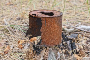 Büyük, kahverengi, paslı, demir bir teneke kutu bir yaz caddesinde gri bir kütüğün üzerinde duruyor.