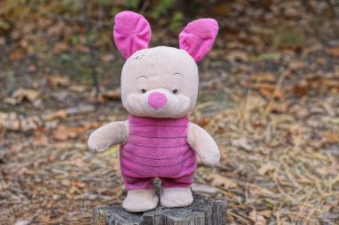 one pink red plush toy pig stands on a gray stump in a summer park clipart