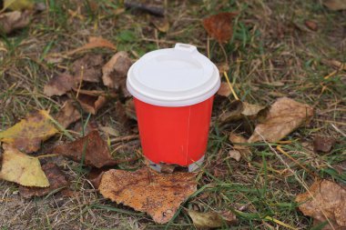 Kapalı kahve, kırmızı kağıt bardak. Plastik kapak, yaz caddesinde yeşil çimlerin üzerinde duruyor.