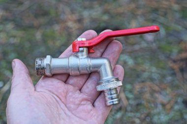 Kırmızı saplı bir metal gri su musluğu yaz sokağında, avucunun içinde duruyor.