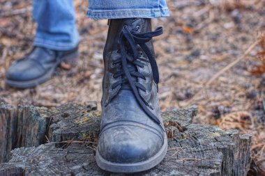 Bir ayaktaki siyah yüksek ordu deri çizmesi doğada gri bir kütüğün üzerinde duruyor.