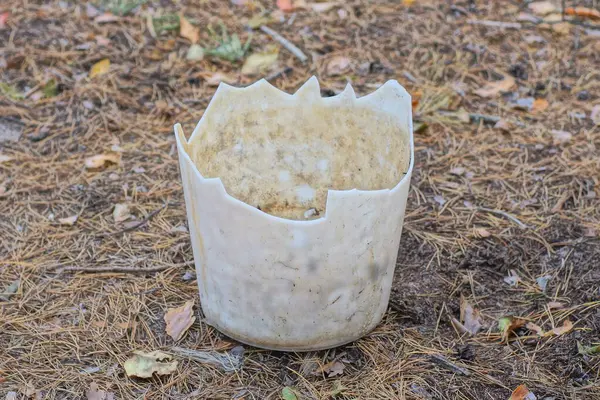 garbage from a piece of a broken white plastic bucket lies on the gray ground on the street