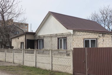 Kırsal beyaz tuğlalı bir ev pencereli ve kiremitli çatı gri beton duvarın arkasında kahverengi metal kapılı yaz caddesinde