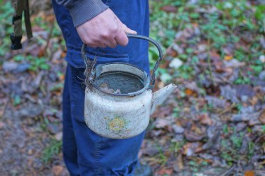 Bir el mavi elbiseli bir adam yaz caddesinde eski beyaz, kirli bir diş minesi boş çaydanlığı tutuyor.