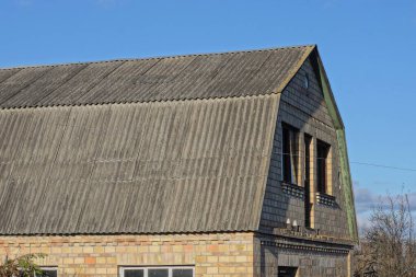 Kırsal kesimde mavi gökyüzüne karşı gri tahta çatılı büyük kahverengi tuğlalı bir evin parçası.