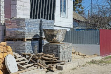 Büyük plastik bir leğen gri kaldırım taşları ve ahşap tahtaların üzerinde duruyor. Yazlık bir caddede, özel bir evin beyaz duvarının yanında.