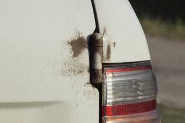 Kirli kapı menteşesi ve yaz caddesinde kırmızı cam stop lambası olan beyaz bir arabanın parçası.