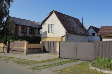 Yazın kırsal kesiminde, duvarları siyah, çitlerle çevrili demir kapı ön cephesi ve güneşli bir günde asfalt yola yakın özel evler mavi gökyüzüne karşı.