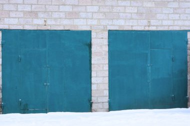 two closed blue metal gates on a gray brick wall of a big garage in white snow in the winter street clipart