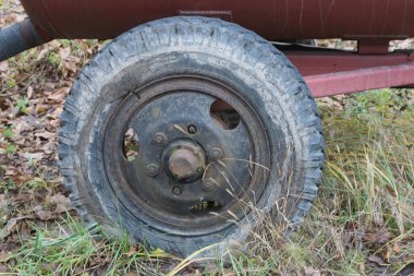 Yeşil çimlerin üzerinde kırmızı demir bir römorkun üzerinde eski bir siyah gri tekerlek.