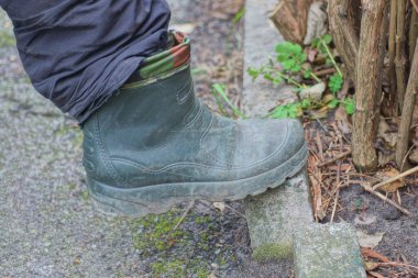 Bir ayağı yeşil lastik bir botun içinde Gri beton kaldırım ve asfalt bir sonbahar caddesinde duruyor
